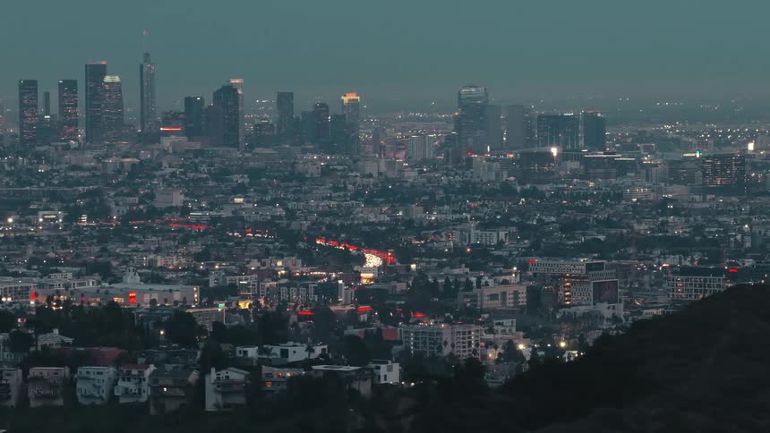 Silhouette of mountains in the foreground and in the background a metropolis illuminated at dusk