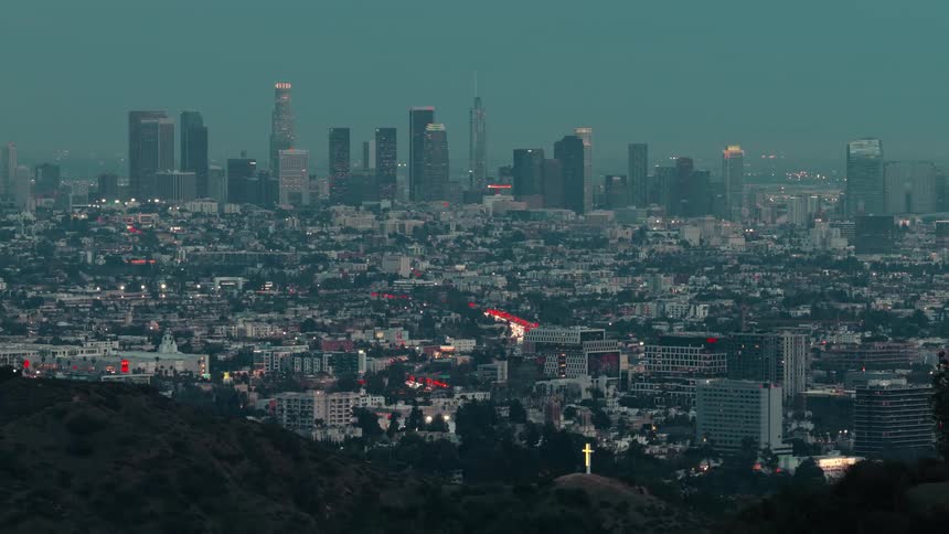 Lit cross atop dark hill facing los angeles skyline at dusk