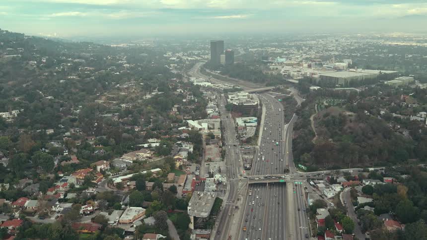 Central highway cutting through treelined residential zone with heavy traffic toward urban horizon