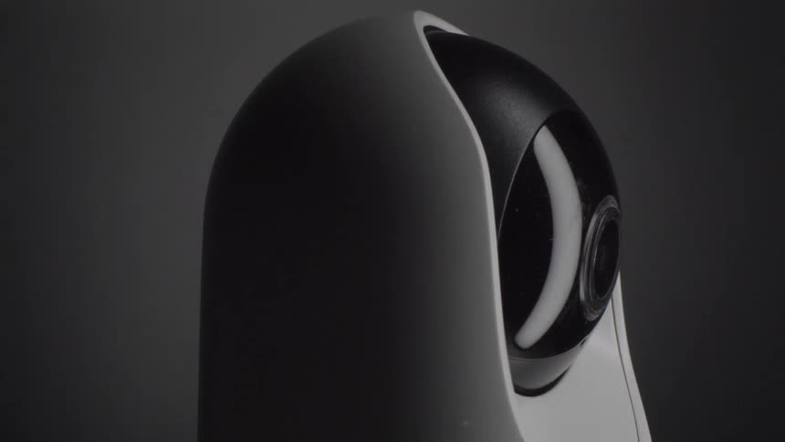 The video shows a sleek modern security camera with a white body and a black spherical lens housing it is captured in a minimalist lowlight setting with a subtle watermark in the center