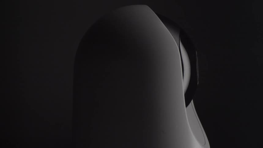 Close view of a white home security camera rotating slowly in a dark environment while being illuminated by a dim light source