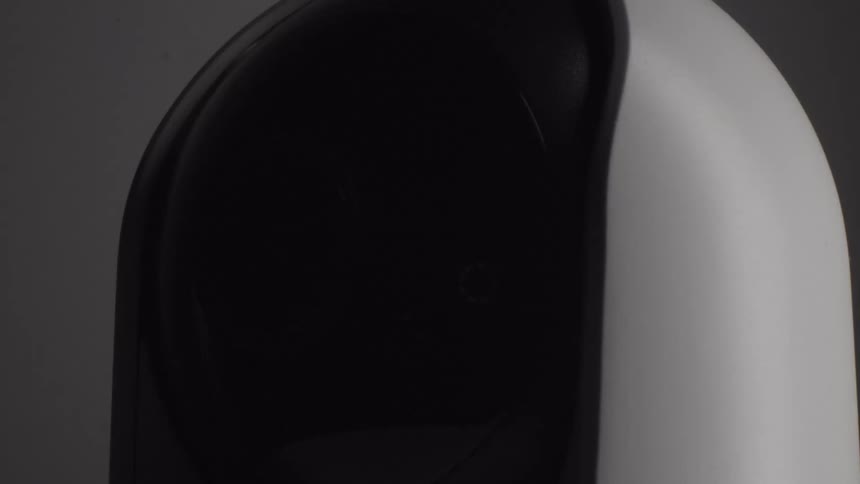 A white and black smart security camera sits against a neutral background as its internal lens housing rotates smoothly to the left