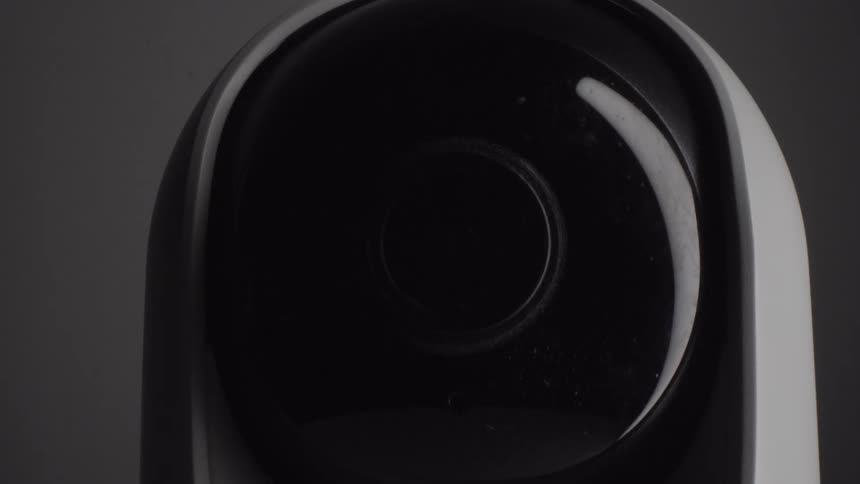 In a closeup studio shot the lens of a black and white smart security camera tilts slowly downward and then back up
