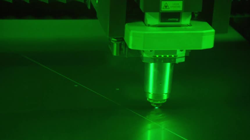 The video shows an industrial laser cutting machine in operation illuminated by a vivid green light as the cutting head moves across the flat metal surface it leaves behind a precise glowing path where the material is being sliced
