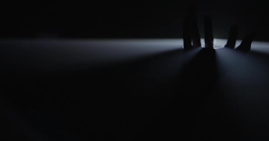 A hand rises through the surface of a light-beam caused by a single light
