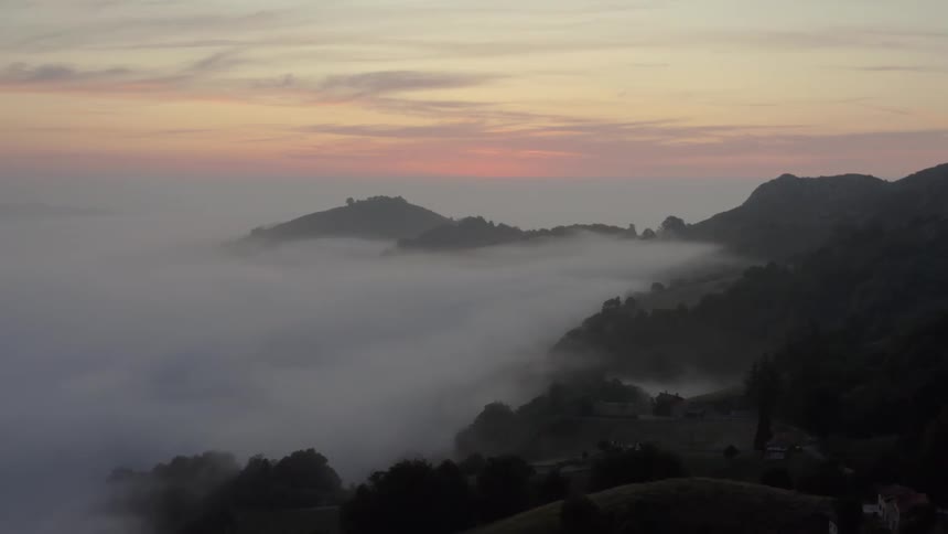 Thick fog fills the mountain valley with houses on the mountainside