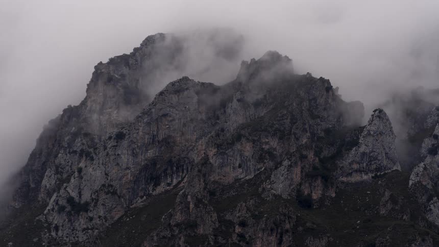 Clouds move over the rough terrain of a rocky mountain