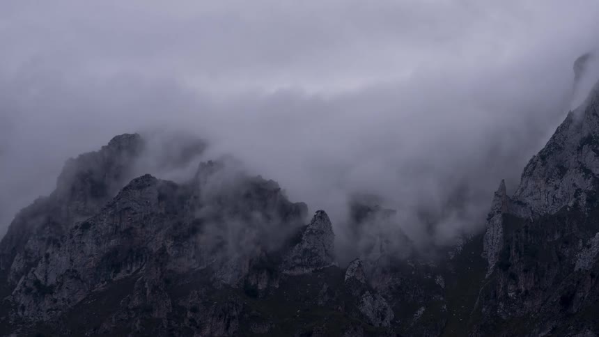 Clouds roll over the rough terrain of mountains
