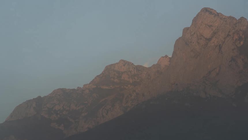 The moon sets behind a mountain as clouds move across the sky
