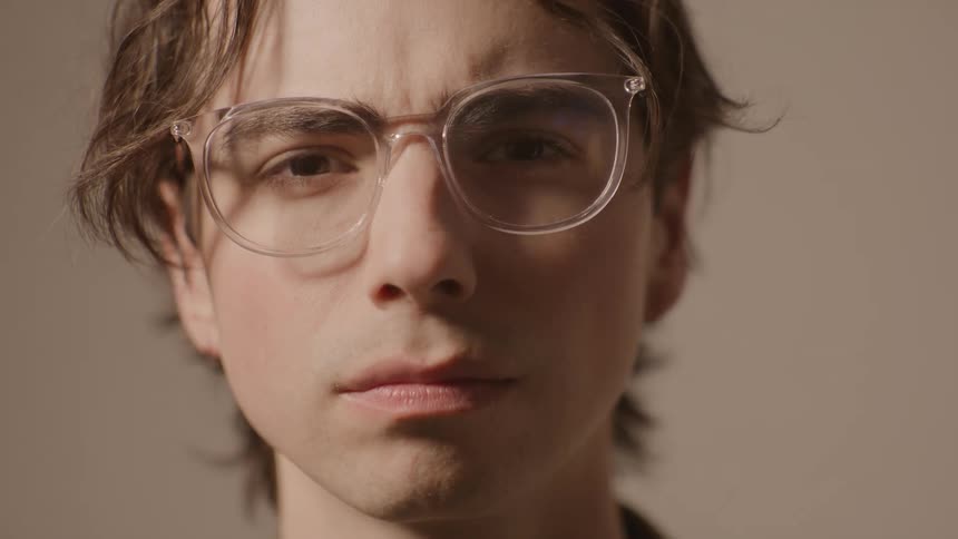 Face with clearframed glasses against beige background with neutral expression