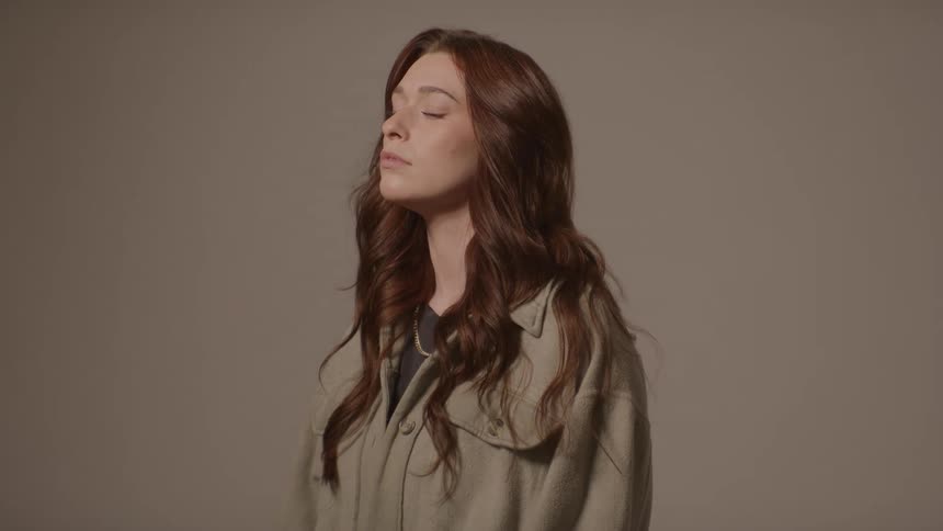 Young adult woman wearing a dress shirt standing with her eyes closed indoors