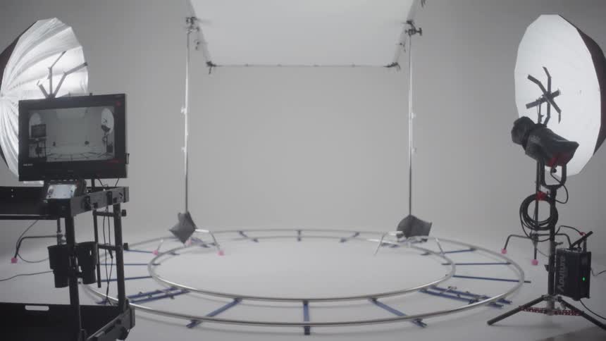 A wideangle view of a professional whitewalled studio featuring a circular floor track surrounded by various lighting rigs softboxes and a monitor station ready for a production