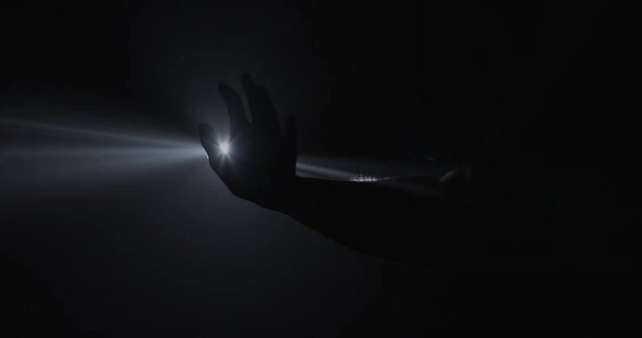 A sharp light reveals the silhouette of a hand and arm