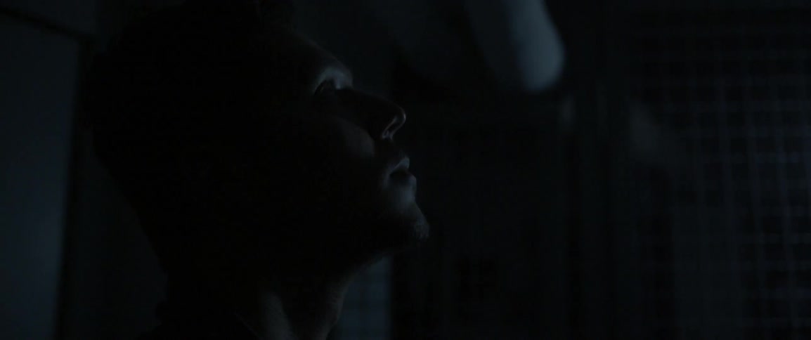 A man sits back looking up in a dark room