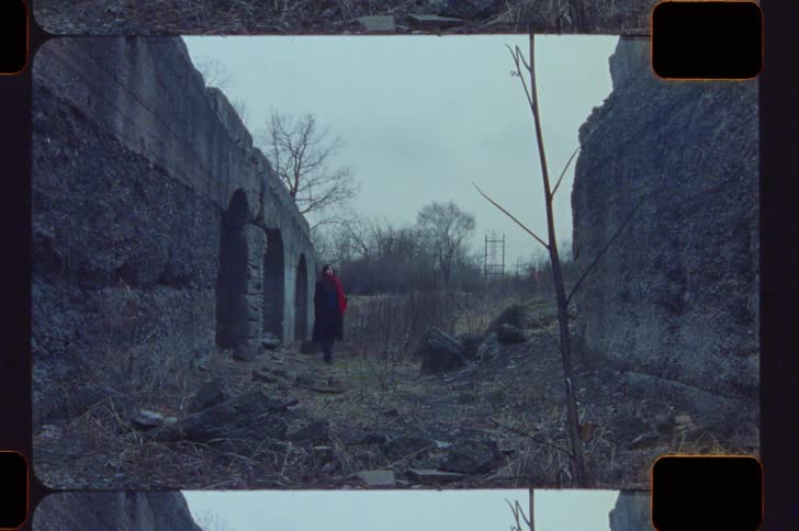 Person in black with red scarf between weathered stone walls