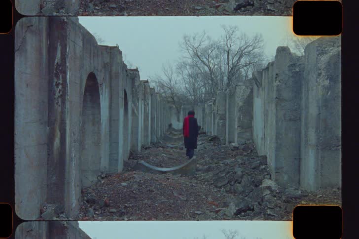 Person walking between weathered concrete walls with red scarf in wintry setting
