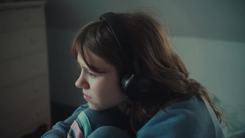 Girl with medium brown hair in blue sweatshirt and large headphones in calm setting
