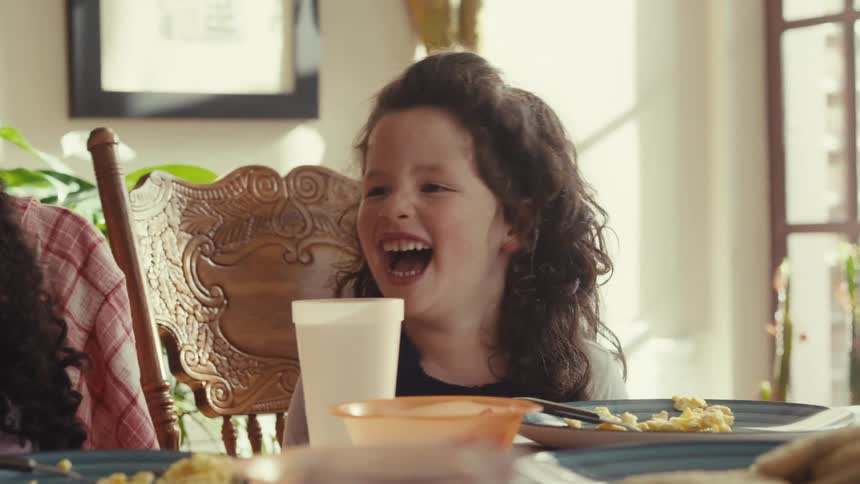 Children smiling during meal at table with plates of scrambled eggs and bread