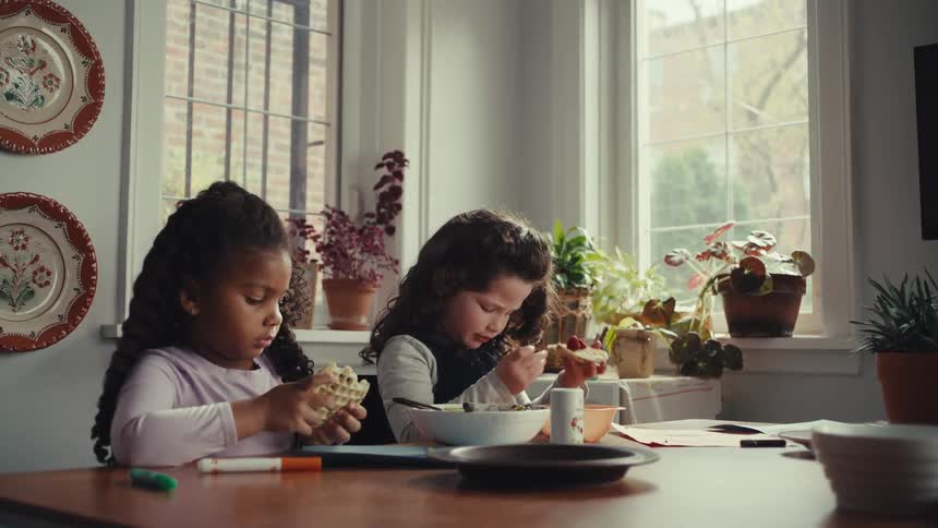 Children seated at table with food and supplies in bright home setting