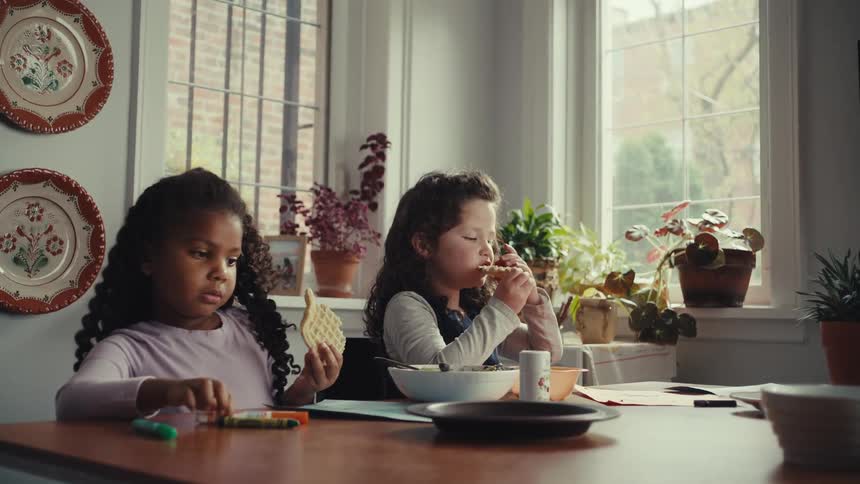 Two young girls sit at the dining table eating muffins for breakfast