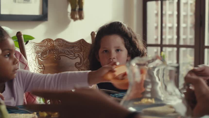 A family eats breakfast together as an adult pours juice into glasses and hands one to a child