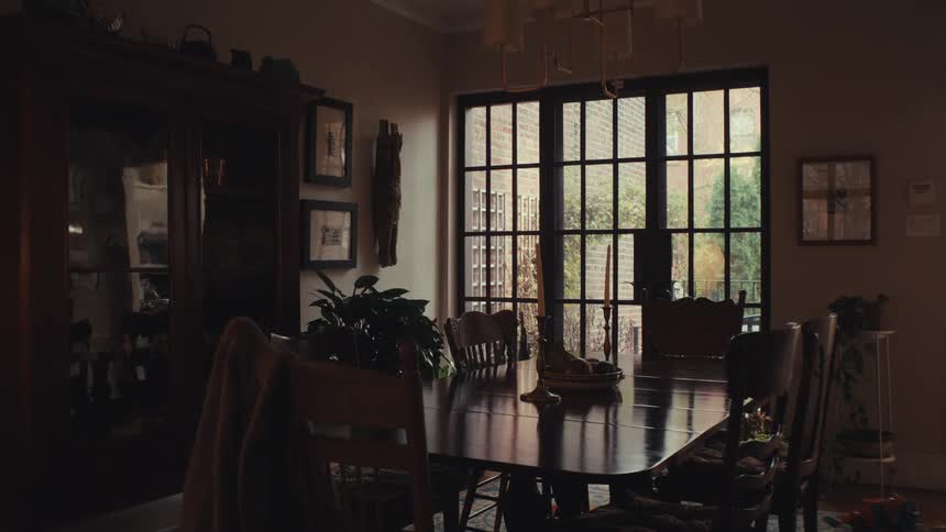 Dining room with central wooden table beneath chandelier in space lit by gridstyle windows