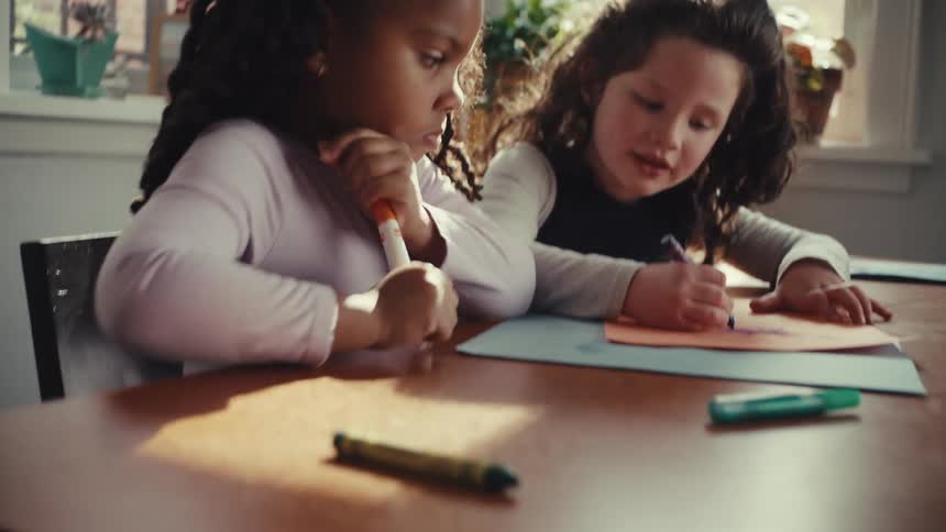 Children drawing with colorful markers at wooden table lit by natural light
