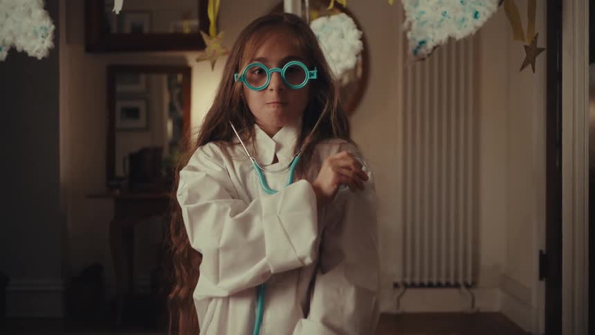 Child with blue glasses and white coat holding toy stethoscope in playful decorated setting