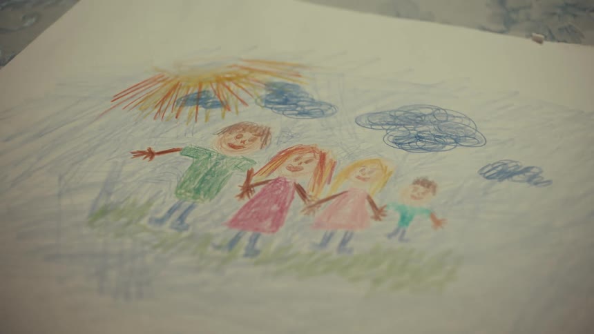 A colorful childs crayon drawing on white paper depicts a family of four holding hands under a bright sun and blue clouds in a simple outdoor scene