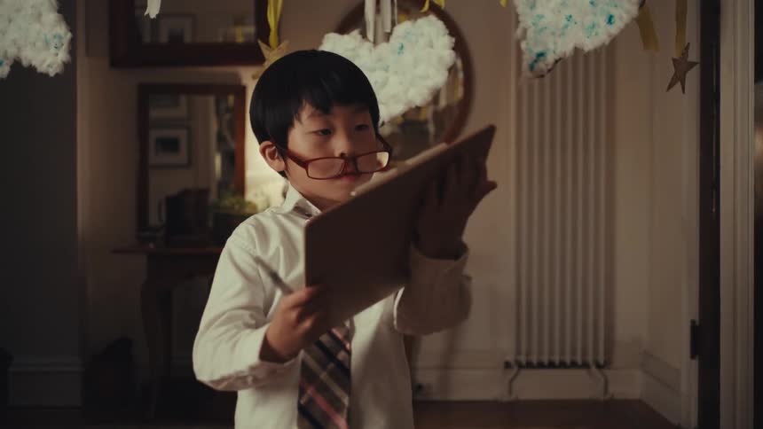 Boy adjusting red glasses with clipboard in hand beneath themed decor with clouds and stars