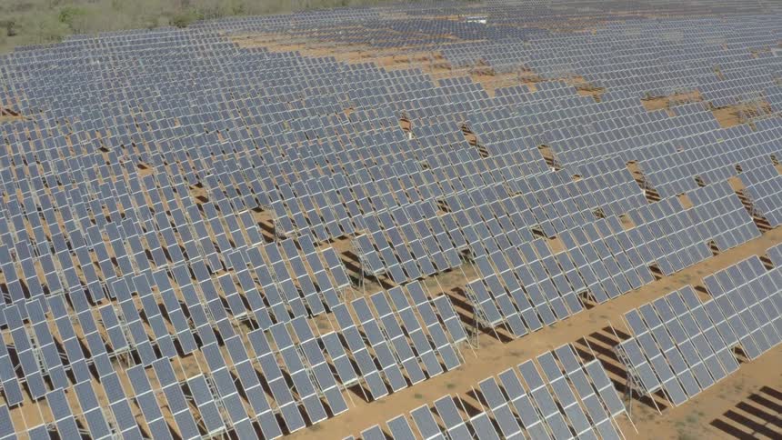 A field filled with solar panels stretches across the landscape on a bright sunny day