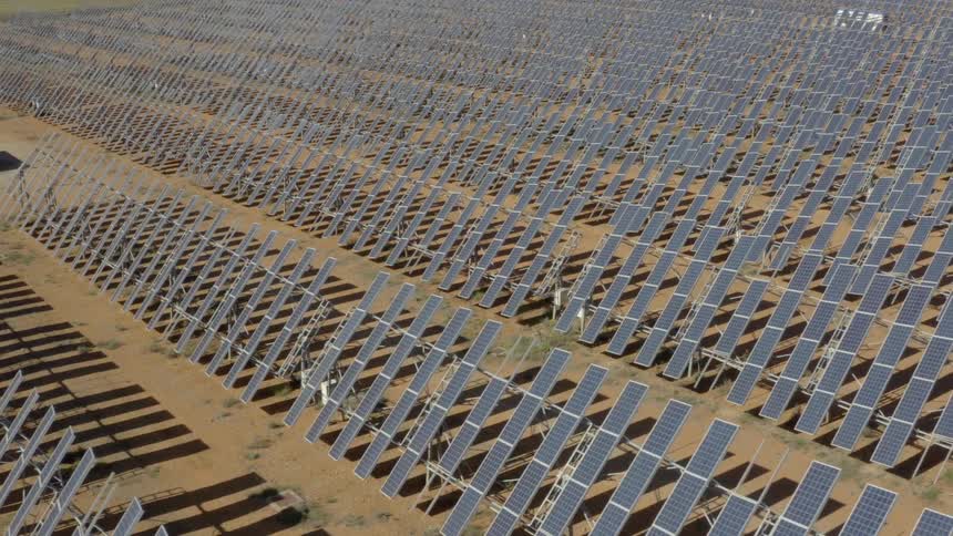 A field covered with solar panels stretches across the landscape generating electricity under a bright sunny sky
