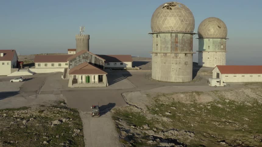 Remote facility with geodesic radar domes on rocky terrain and sparse vegetation