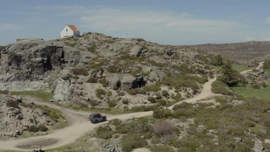 Black suv on winding dirt road heading toward solitary white house atop rocky hill