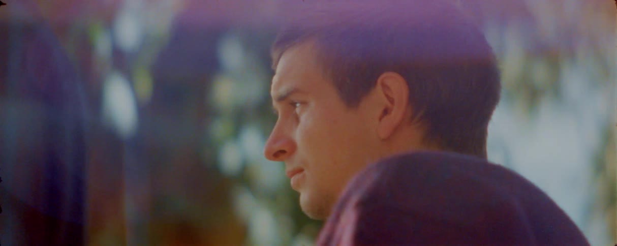 A man is shown in a closeup profile view looking off to the side with a contemplative expression the shot features a warm hazy lighting effect with soft lens flares and a blurred natural background