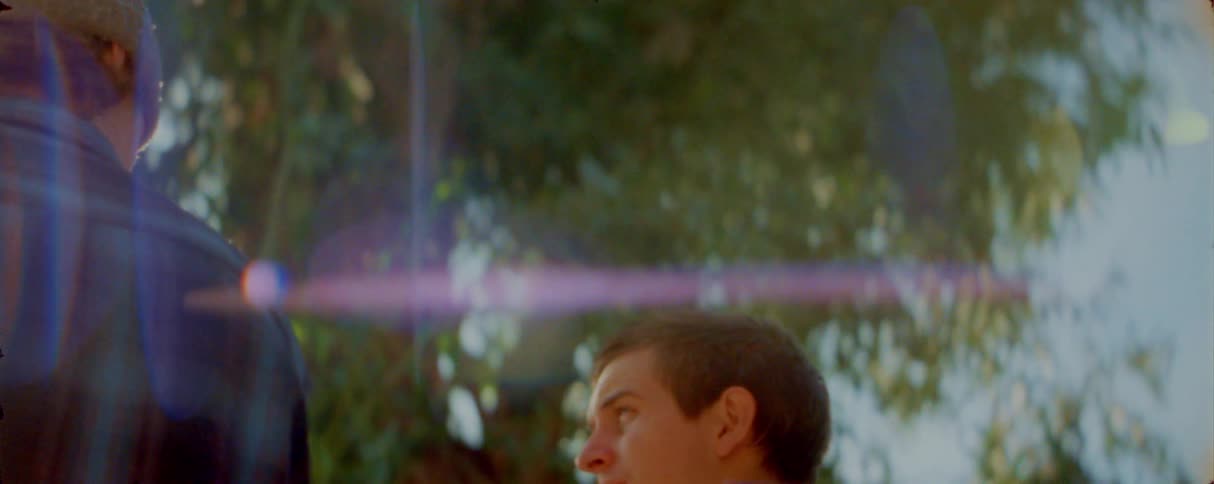 A young man looks up thoughtfully while talking to someone outdoors