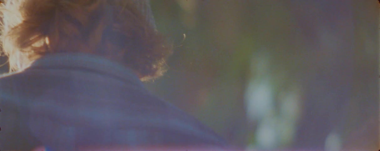 A hazy sundrenched sequence follows a young mans profile as the camera shifts focus to the back of another man knitcapped head amidst a soft purple lens flare and bright natural light