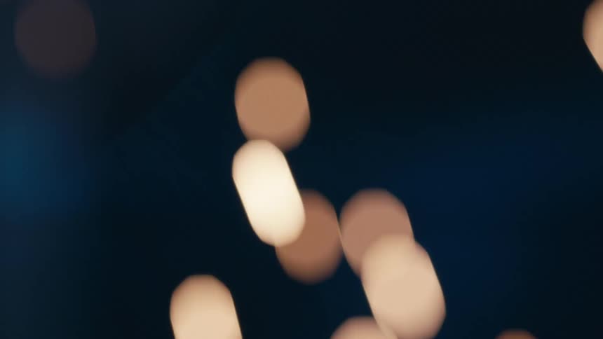 Bright orange sparks and glowing embers rise and drift upward against a deep blue dark background gradually softening into blurry bokeh circles as they move out of focus