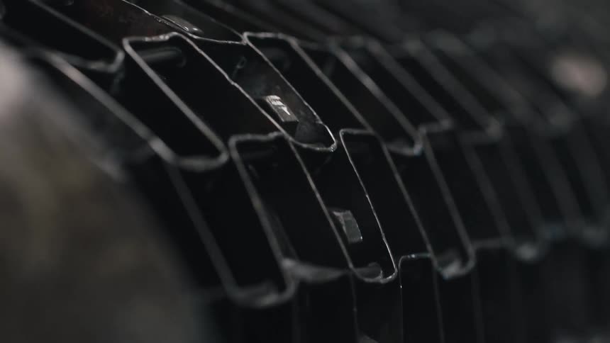 A dark metallic industrial structure consisting of a gridlike pattern rotates slowly in a shallow depth of fieldtiny sparks or reflective particles flick across the dark textured surface as the mechanism moves steadily