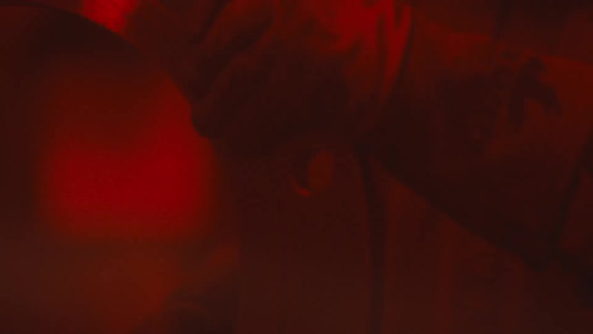 A brilliant shower of red sparks erupts from a grinding machine before a gloved hand moves in to work on a metal part all under intense crimson lighting