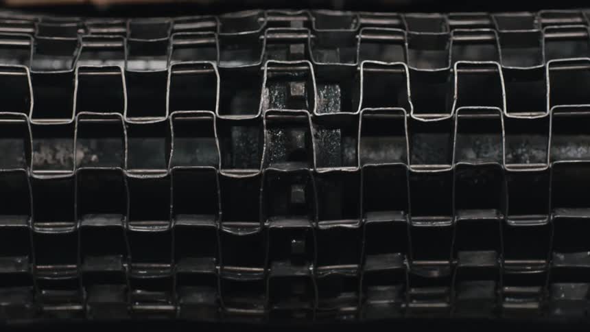 A dark grid patterned industrial metal roller turns slowly in a close up shot