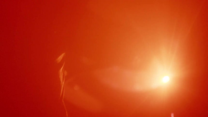 Intense light passes through a red medium forming curved reflections and illuminated particles