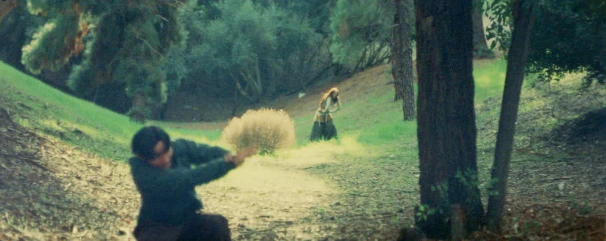 Person performs dance movements on a wooded path during daylight