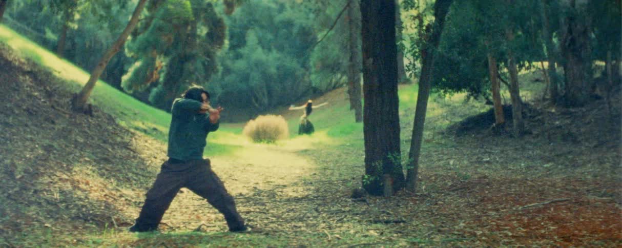 Teenager boy making dance moves next to a female person some feet away behind him in an area surrounded by trees outdoors during day time