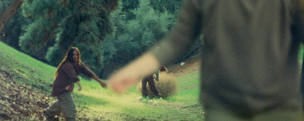 Three people dance freely in a sunlit grassy clearing in the woods