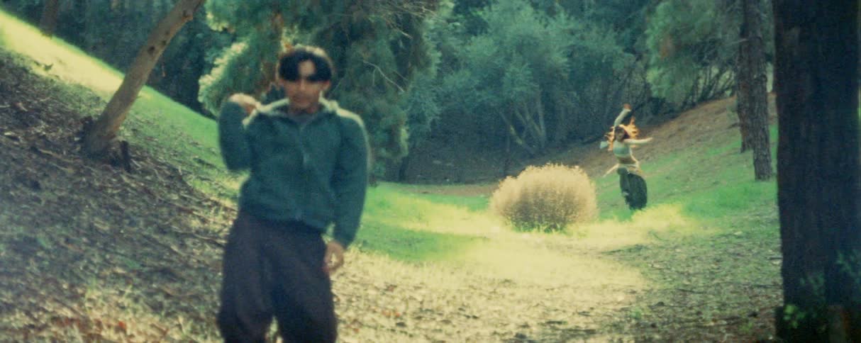 A young man and woman dancing on a field outdoors in a woodland area during daytime