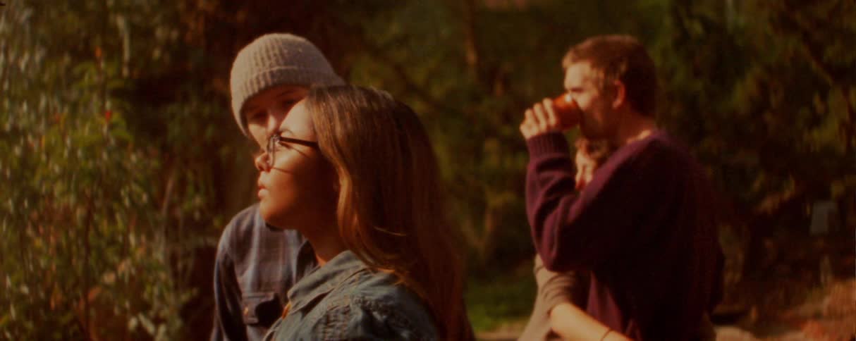 Adult people stand together outdoors with vegetation and warm lateafternoon lighting