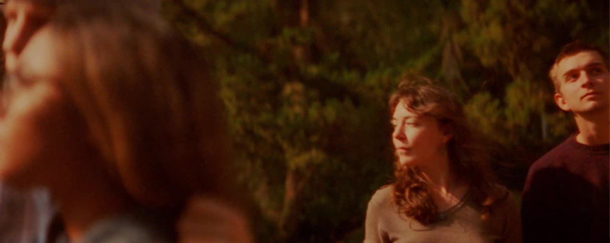 A young couple walks through the woods at midday the woman holding a coffee cup as they come upon another couple who is quietly admiring the surrounding nature