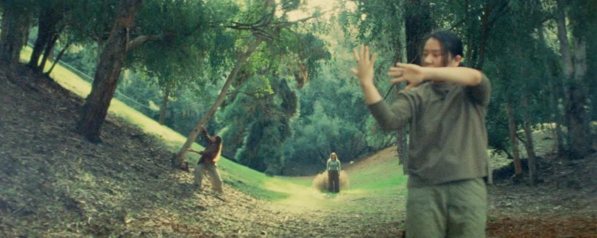 Three people perform a synchronized contemporary dance routine in a wooded clearing focusing on fluid arm gestures and torso shifts while spaced apart on a leafcovered slope