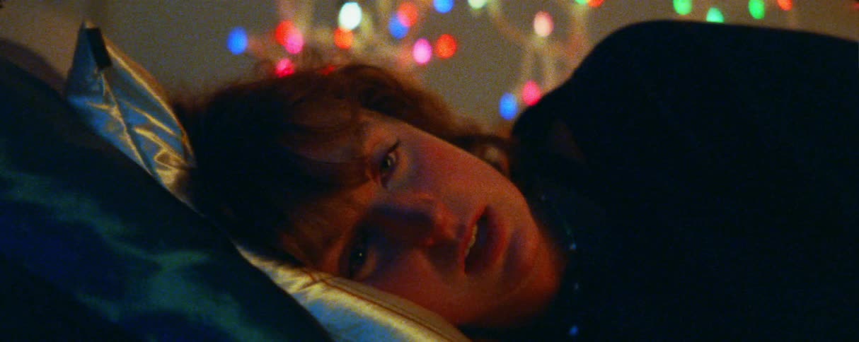 A person lies in bed with their eyes partially open appearing to be in a state of rest or deep thoughtcolorful outoffocus lights glow in the background creating a soft and warm atmosphere around them